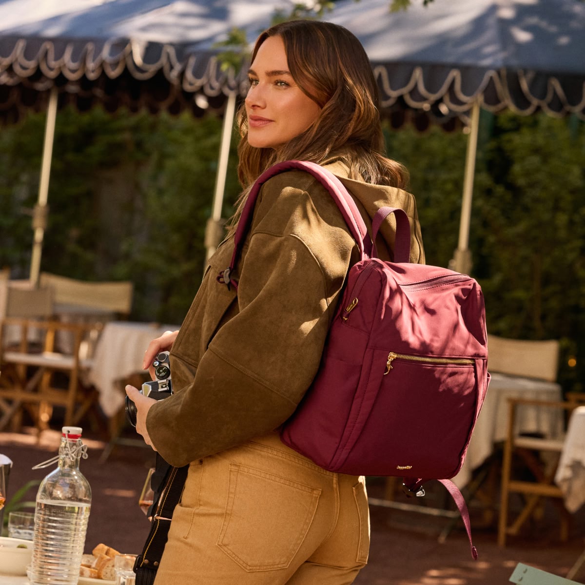 Woman outdoors wearing a burgundy Baggallini anti-theft backpack with gold hardware.