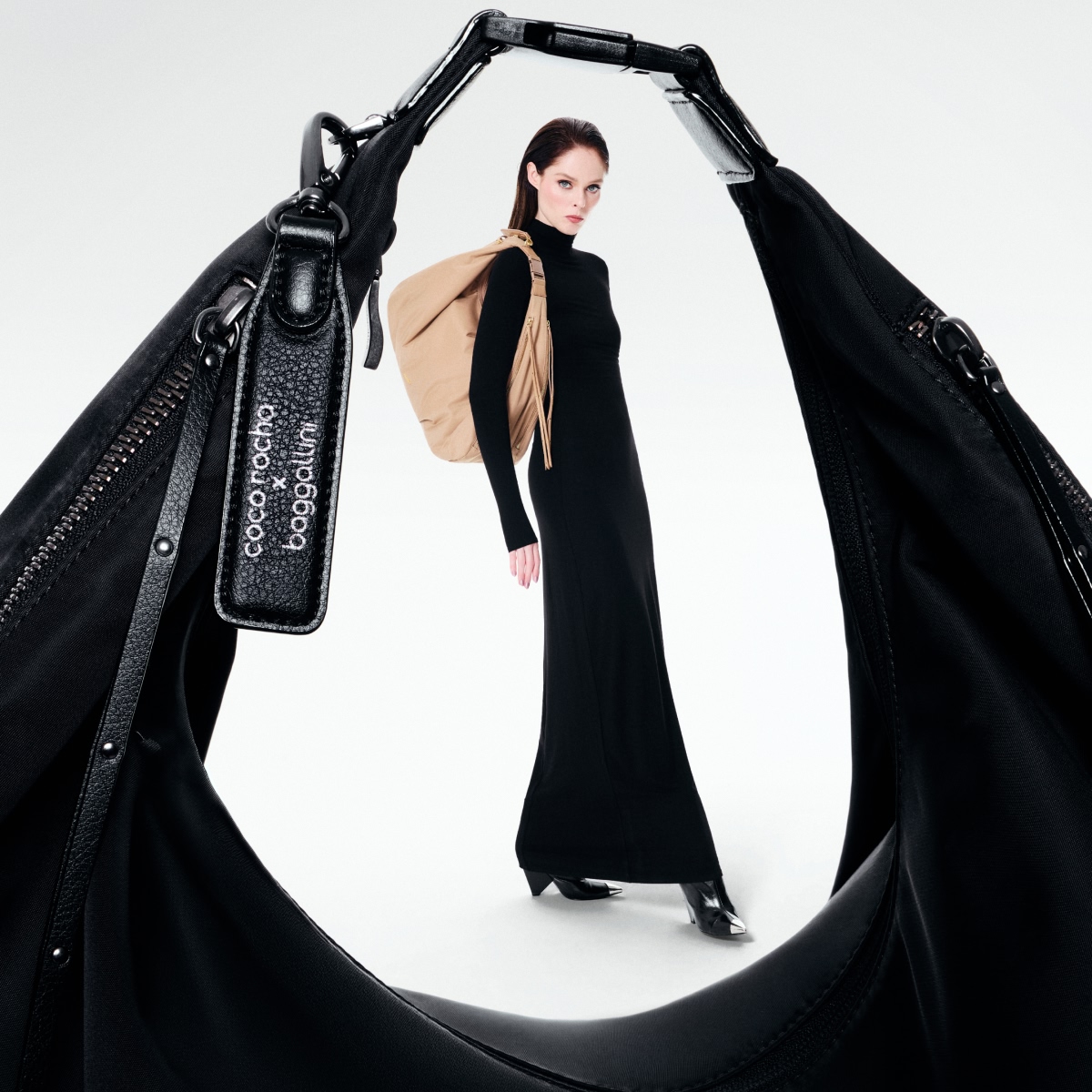 Model Coco Rocha in black holding a tan Baggallini bag, framed through an oversized black bag.