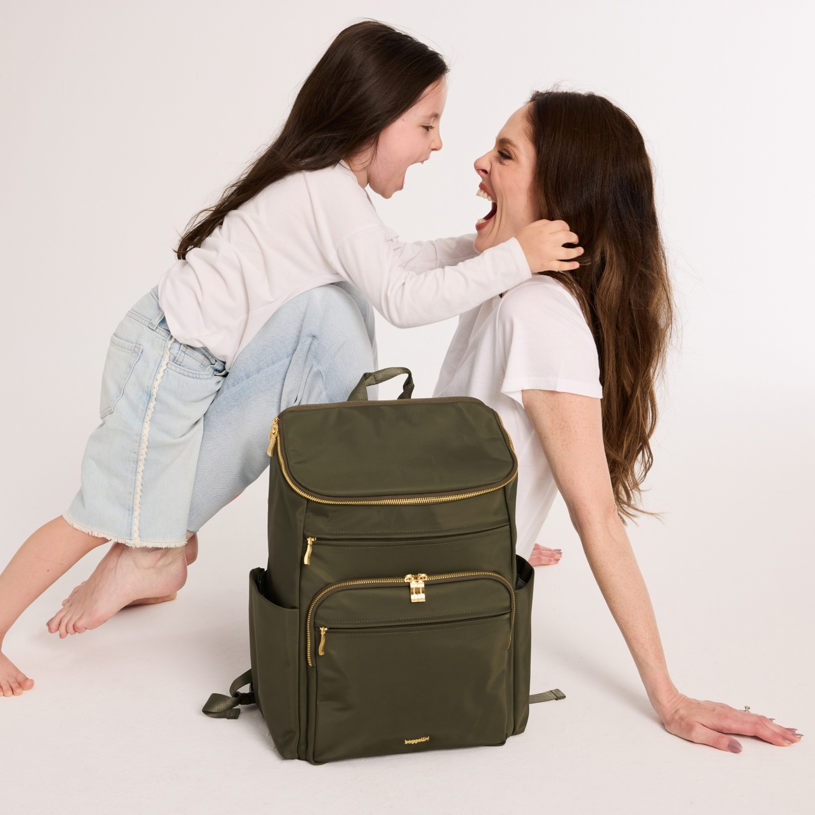 Coco Rocha and her daughter laughing together beside an olive green Baggallini backpack.