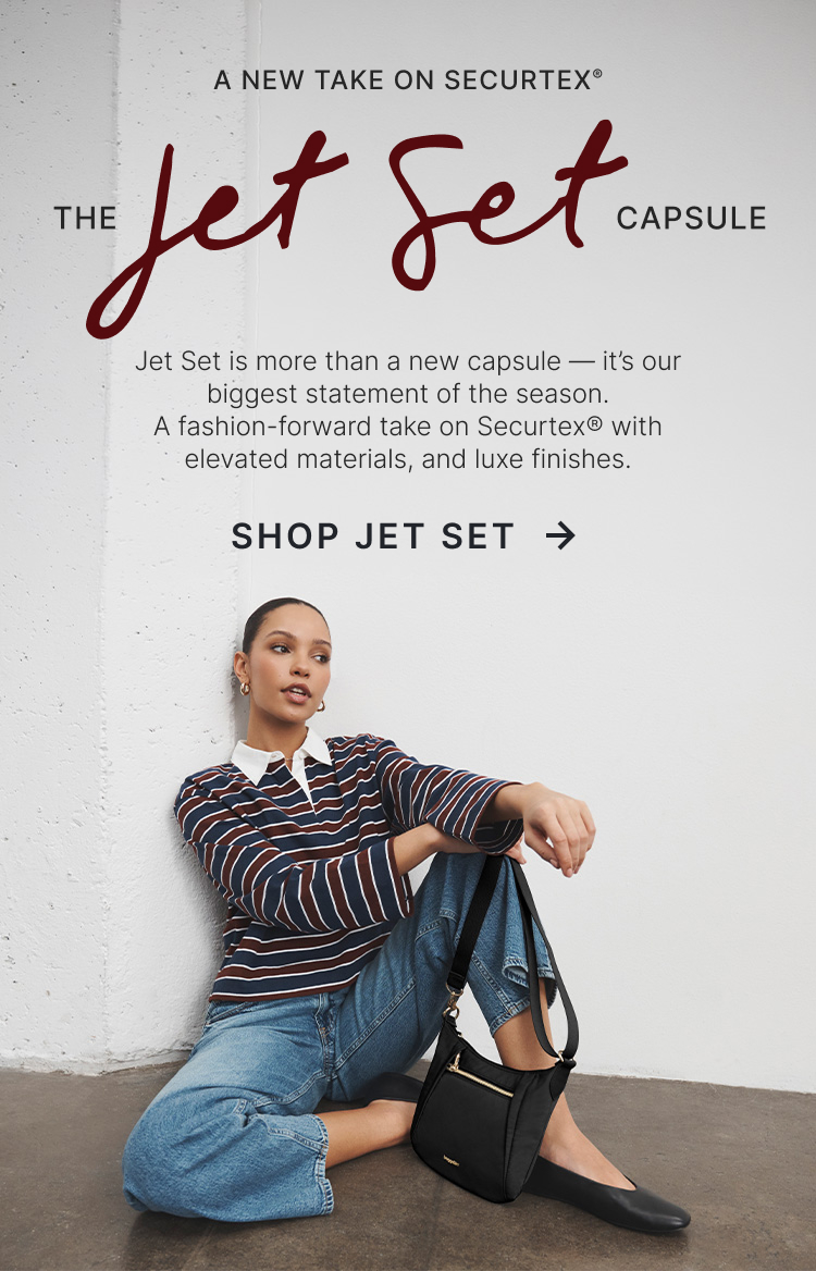 Model seated against a white wall wearing the Jet Set Crossbody from Baggallini's Jet Set capsule featuring elevated anti-theft design.